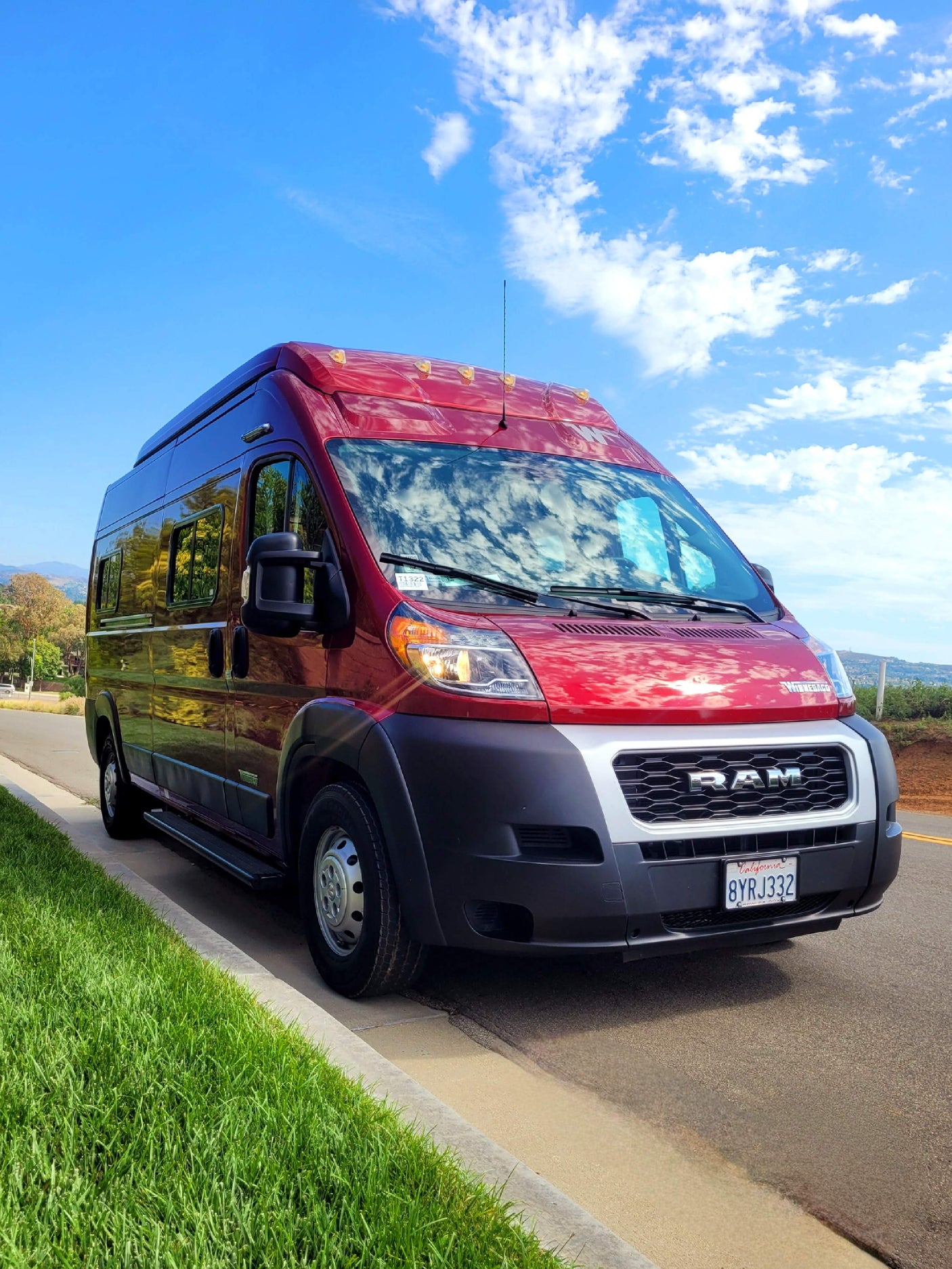 Stylish red Ram ProMaster RV rental parked curbside on a sunny day. Ready for adventure!