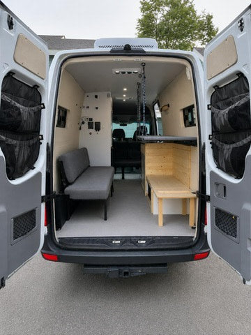 RV rental camper van interior. Rear doors open to reveal bench seating, storage, and a suspended bed, ready for adventure.