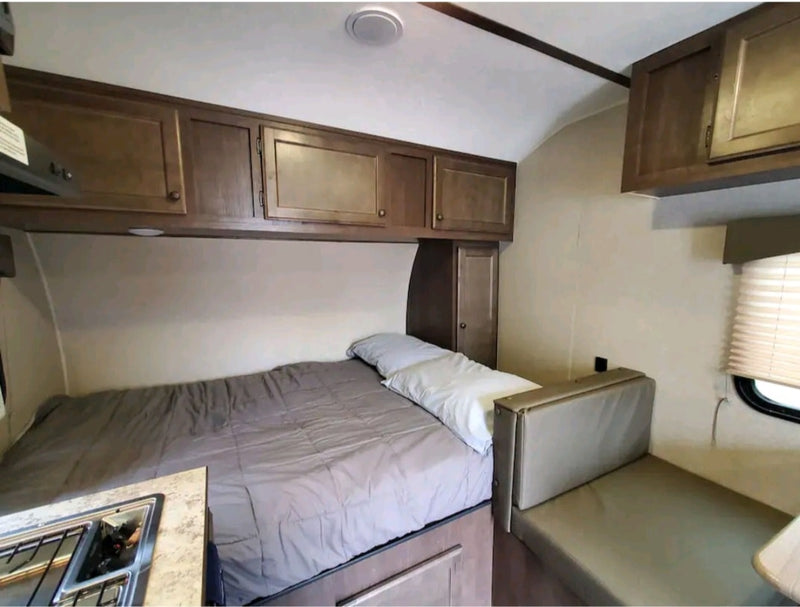Cozy RV rental bedroom setup with a bed, overhead wood cabinets, a compact kitchenette, and a sofa/dinette area. — photo 11