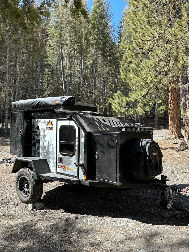 An Off Grid Expedition 2.0 camper trailer, like an RV rental, parked in a sunny forest setting. — photo 10