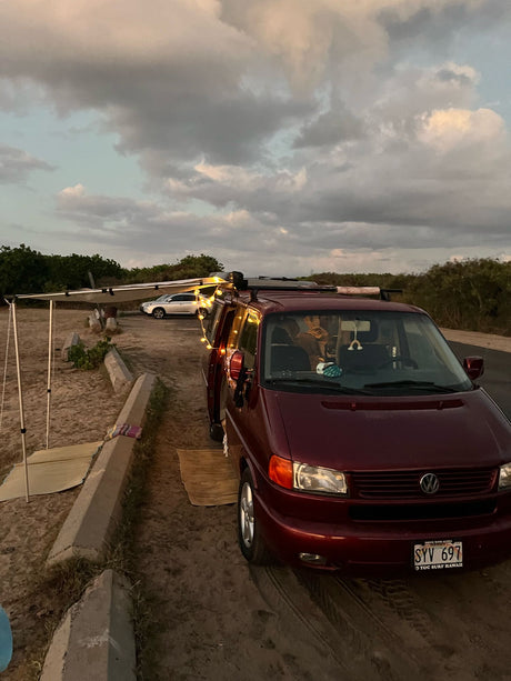 Maroon VW camper van set up for beach camping with string lights & awning. Perfect RV rental for Hawaii adventures!