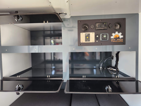 Inside an RV rental: control panel with inverter remote & heater, plus storage compartments and utility hookups. Off Grid Trailers.