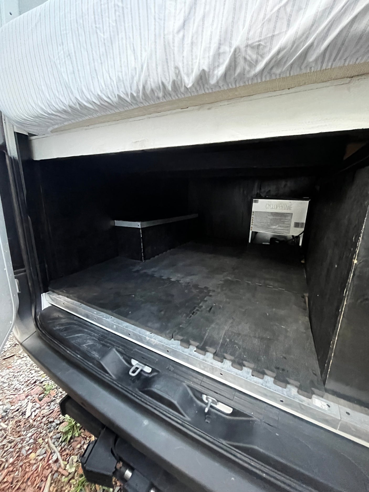RV rental's rear storage area: black floor mats, a raised shelf, and a bed platform directly above, ready for gear.
