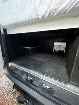 RV rental's rear storage area: black floor mats, a raised shelf, and a bed platform directly above, ready for gear.