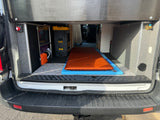 Rear interior of a custom RV rental camper van, showing a comfy bed, organized storage, and essential utilities.