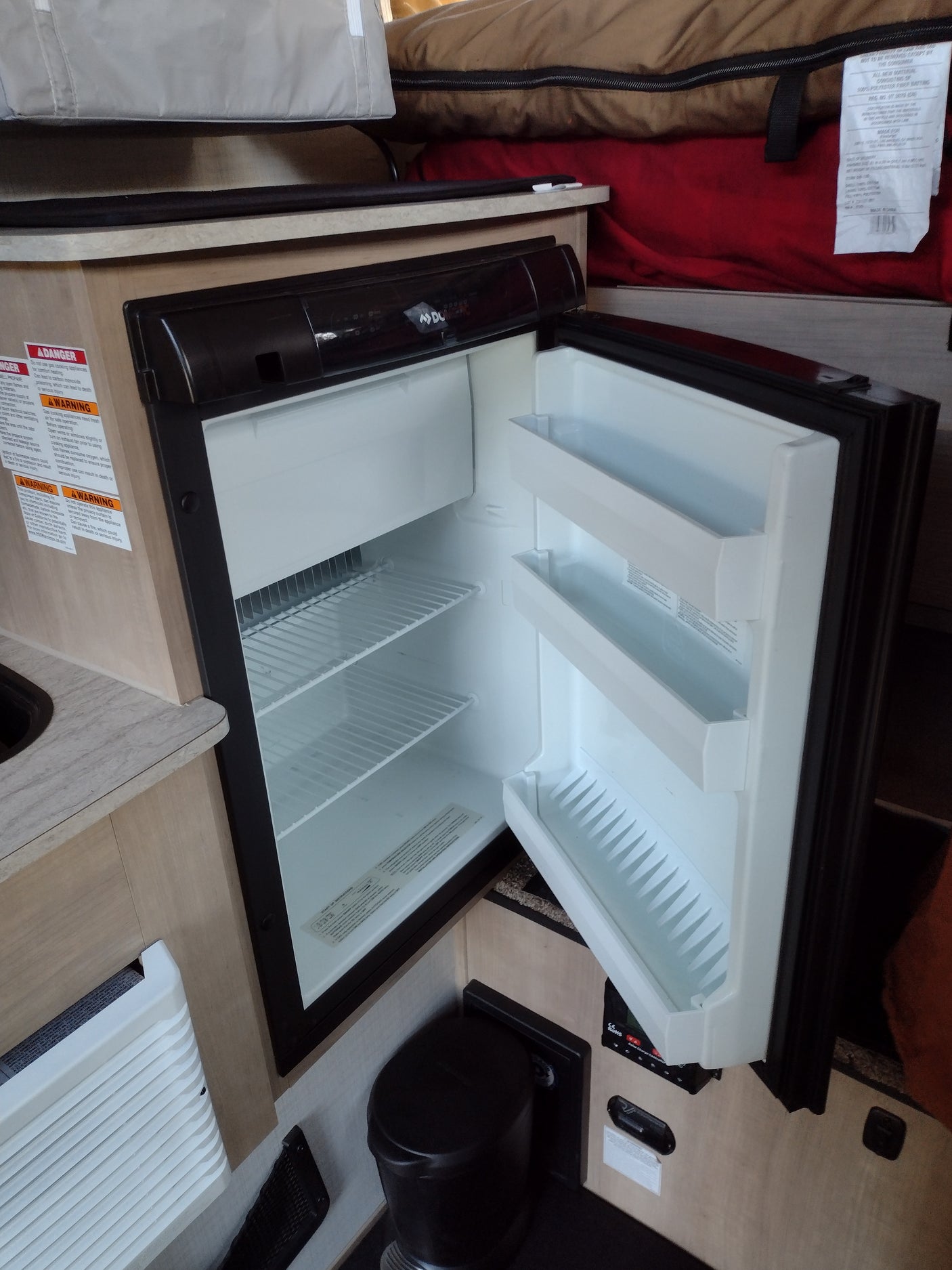 Open refrigerator in an RV rental, showcasing a compact camper kitchen, sleeping area, and essential onboard appliances.