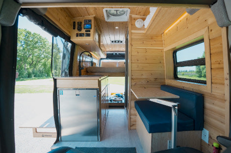 Modern RV rental interior: wood-paneled walls, kitchen with fridge, cozy dinette, & bright window. Perfect for adventures.