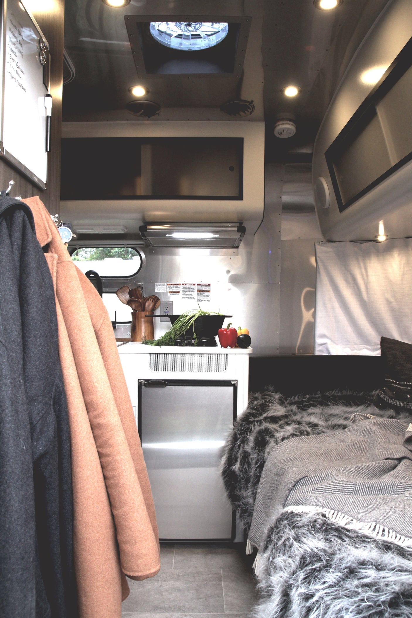 Inside a stylish RV rental: kitchenette with fresh produce, mini-fridge, and a comfy bed with cozy blankets.