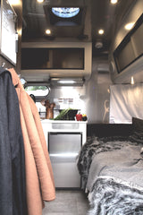 Inside a stylish RV rental: kitchenette with fresh produce, mini-fridge, and a comfy bed with cozy blankets.