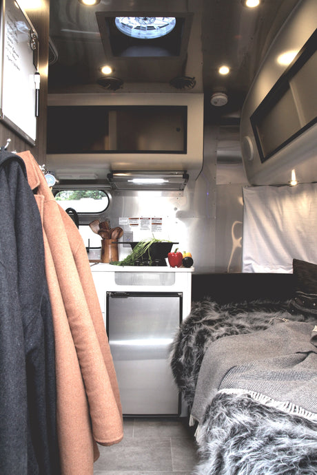Inside a stylish RV rental: kitchenette with fresh produce, mini-fridge, and a comfy bed with cozy blankets.