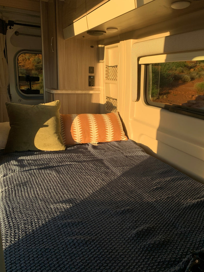 Cozy RV rental interior with a bed, pillows, and warm sunlight from the window revealing an arid landscape. — photo 8