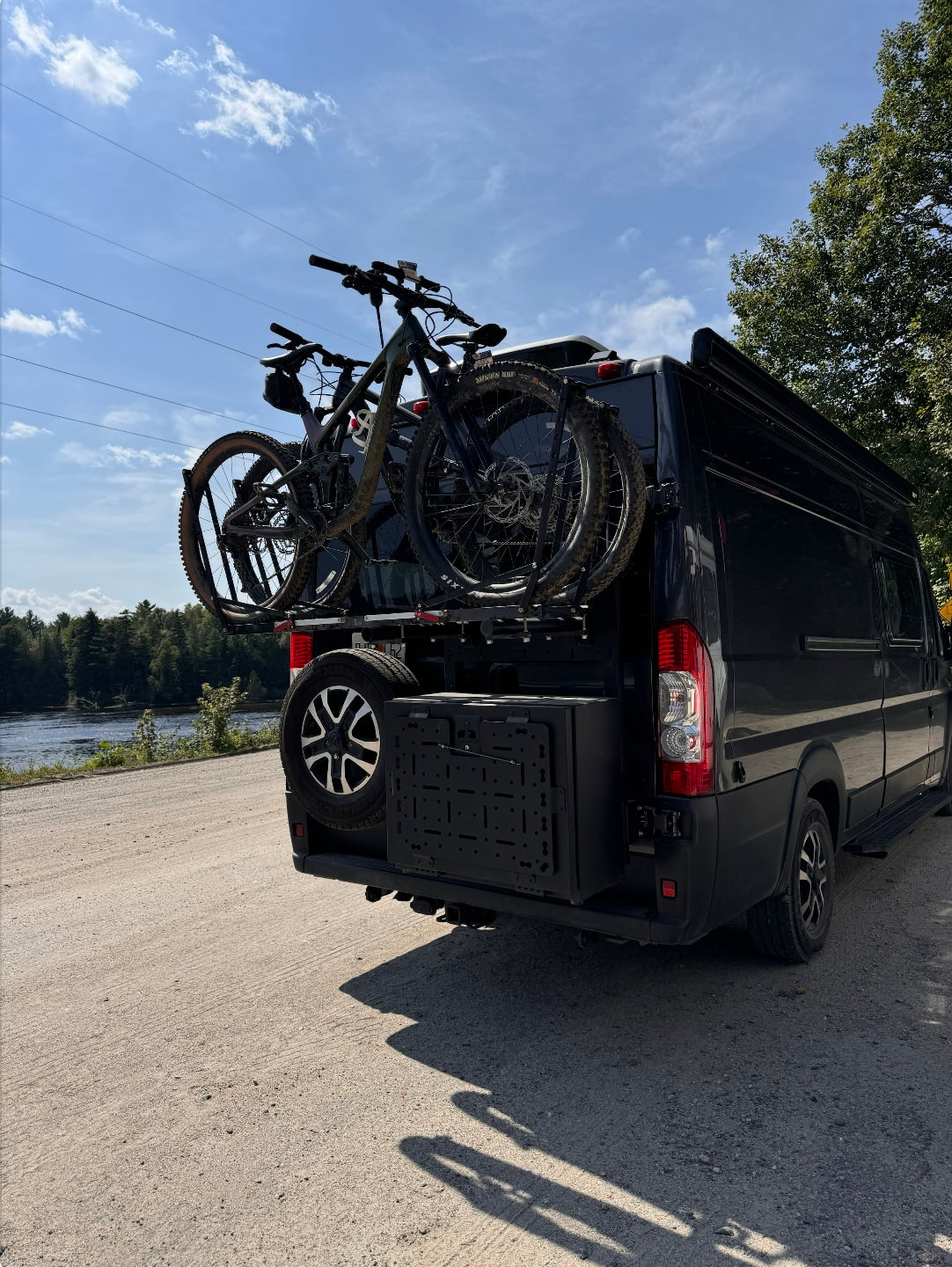 Black camper van on dirt road, carrying two mountain bikes & spare tire. Ideal for an rv rental adventure!