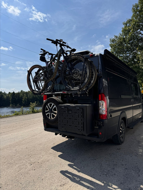 Black camper van on dirt road, carrying two mountain bikes & spare tire. Ideal for an rv rental adventure!