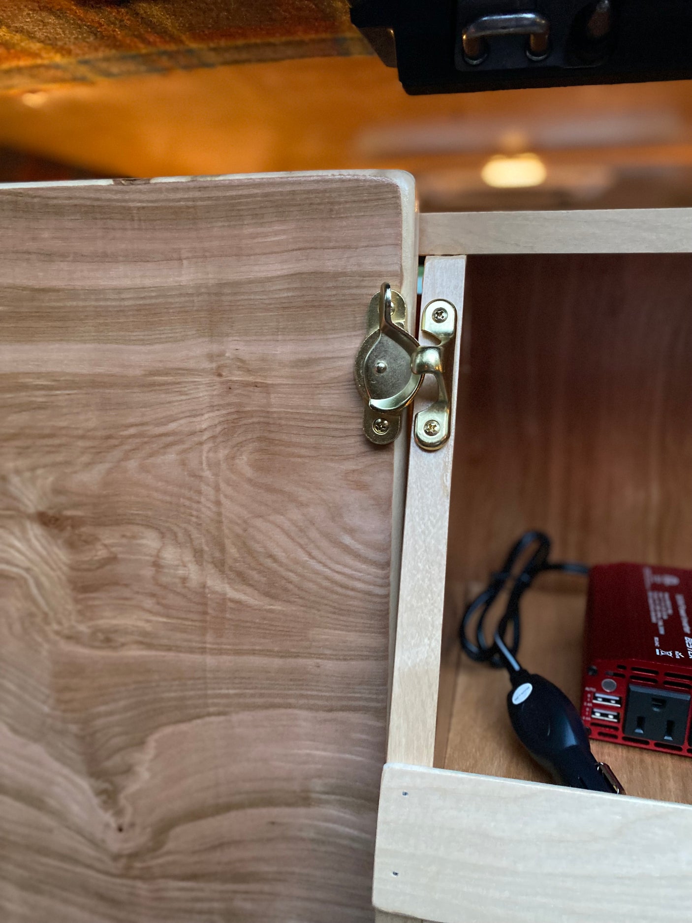 This RV rental's wooden cabinet features a brass latch, opening to reveal a power inverter for your off-grid needs.