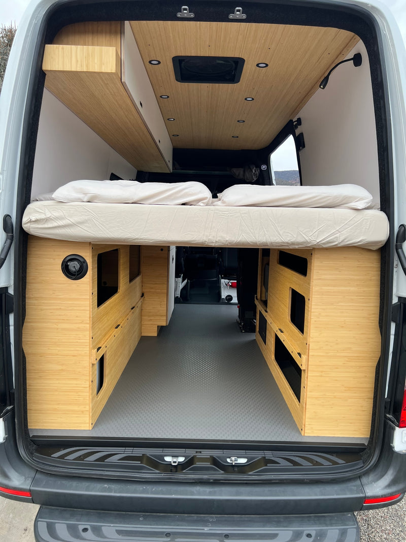 Inside a stylish rv rental: raised bed, sleek bamboo storage, ceiling fan, and textured floor for comfortable travel. — photo 16