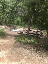Relaxing at a shady forest campsite with picnic tables and fire pit. Perfect for your next RV rental adventure.