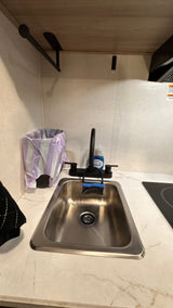 This RV rental kitchen features a modern sink, black faucet, soap, sponge, trash can, and clean marble-look countertop with a cooktop.