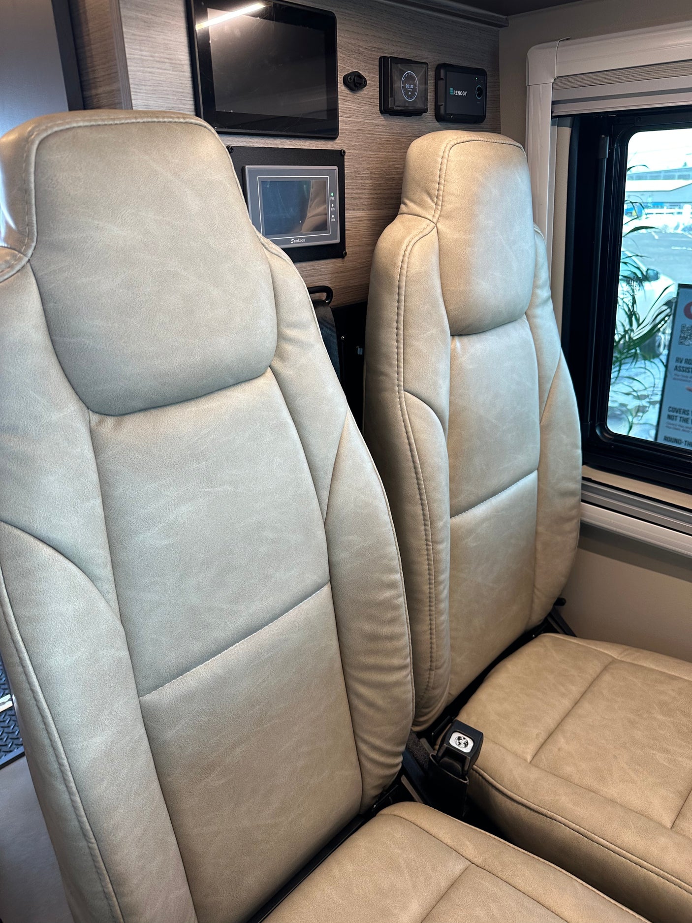 Modern RV rental interior: two plush seats, window view, and smart control panels for comfortable travel.