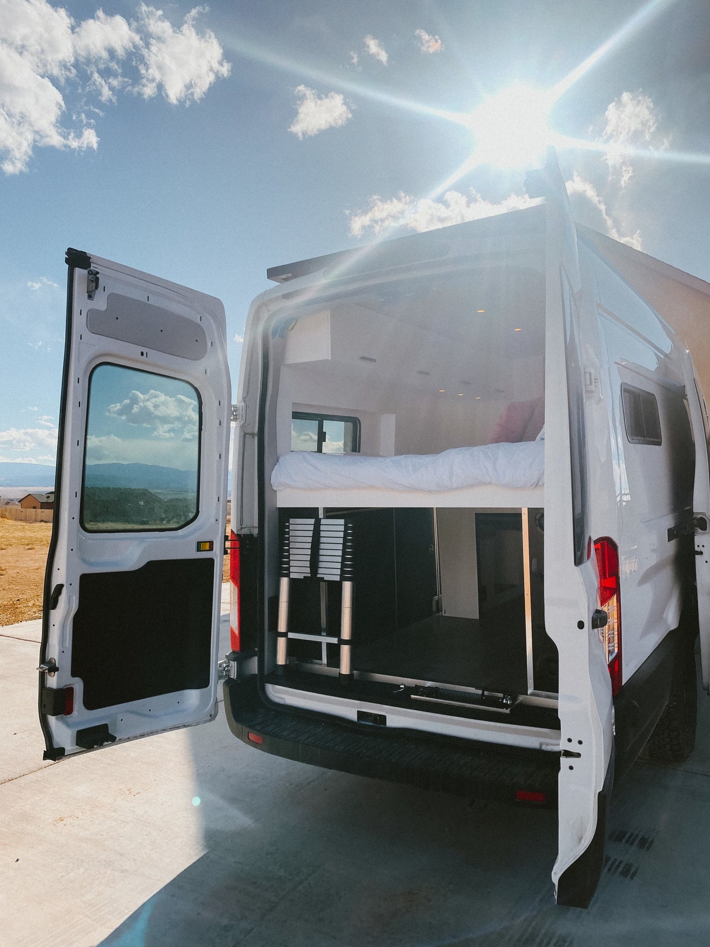 Explore our RV rental camper van's interior! Rear doors open to reveal a comfy bed, storage, and ladder, perfect for sunny day travel. — photo 10