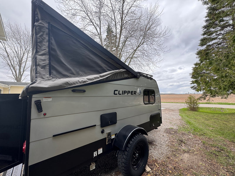  and hitch.|Grey pop-up RV rental with 'Clipper' branding and partially extended canvas roof for travel adventures.|RV rental power inlet. Side view of a black electrical inlet with three metal prongs (two flat — photo 7