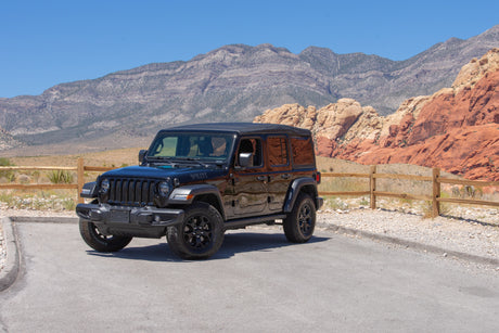 A black Jeep Wrangler in a desert landscape with red rocks, perfect for exploring adventure destinations often sought by RV rental travelers.