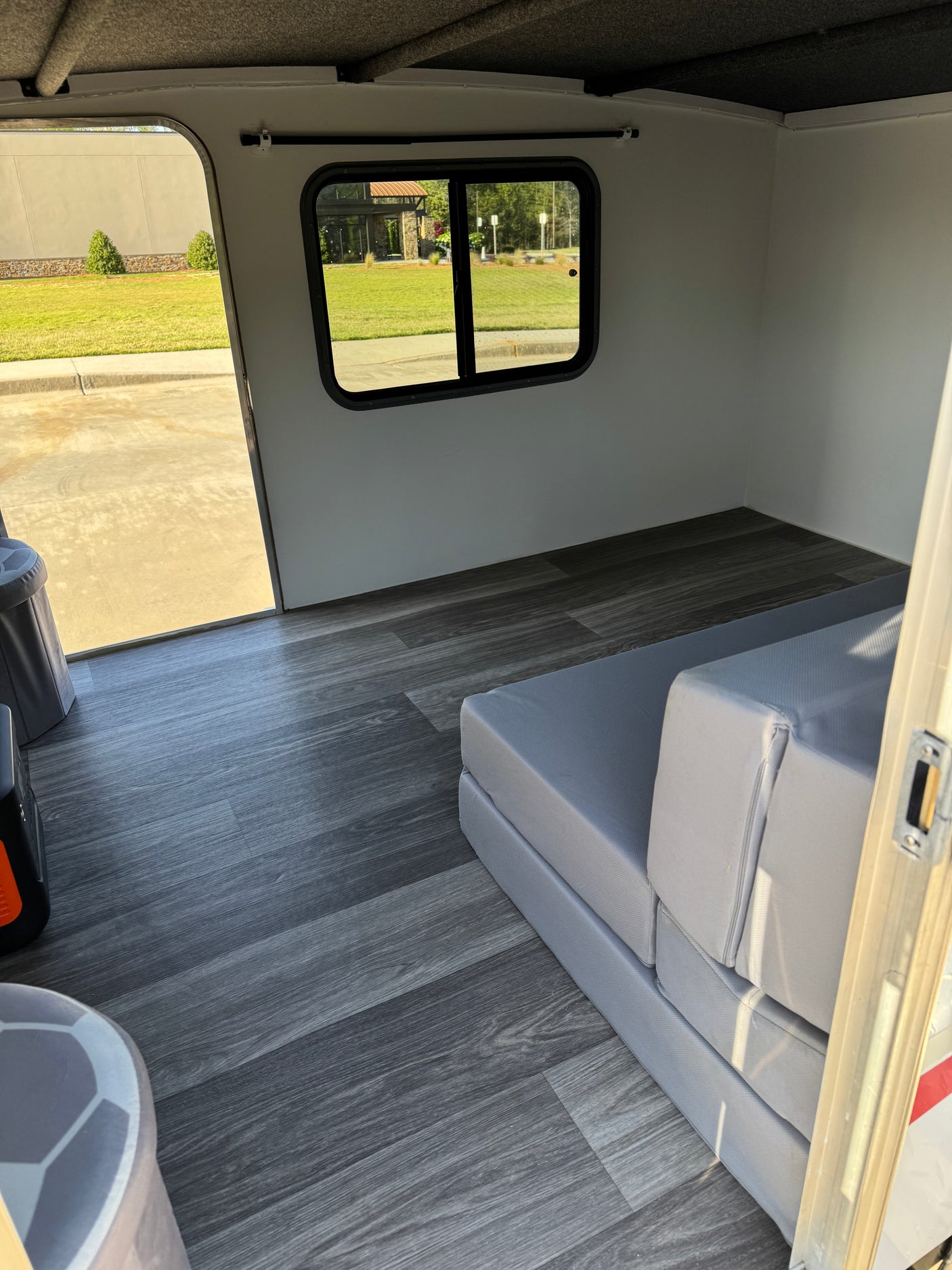 Clean RV rental interior with grey flooring, window view, and foldable bed. Ideal for compact travel.