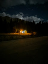Cozy RV rental illuminated at night in a mountain forest setting, perfect for camping under the stars.
