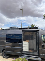 Dark grey camper van, an ideal RV rental, with its side door open showing a modern interior and rooftop AC/solar panels.
