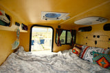 Cozy RV rental interior with a comfy bed, colorful pillows, and a scenic outdoor view. Perfect for camping.