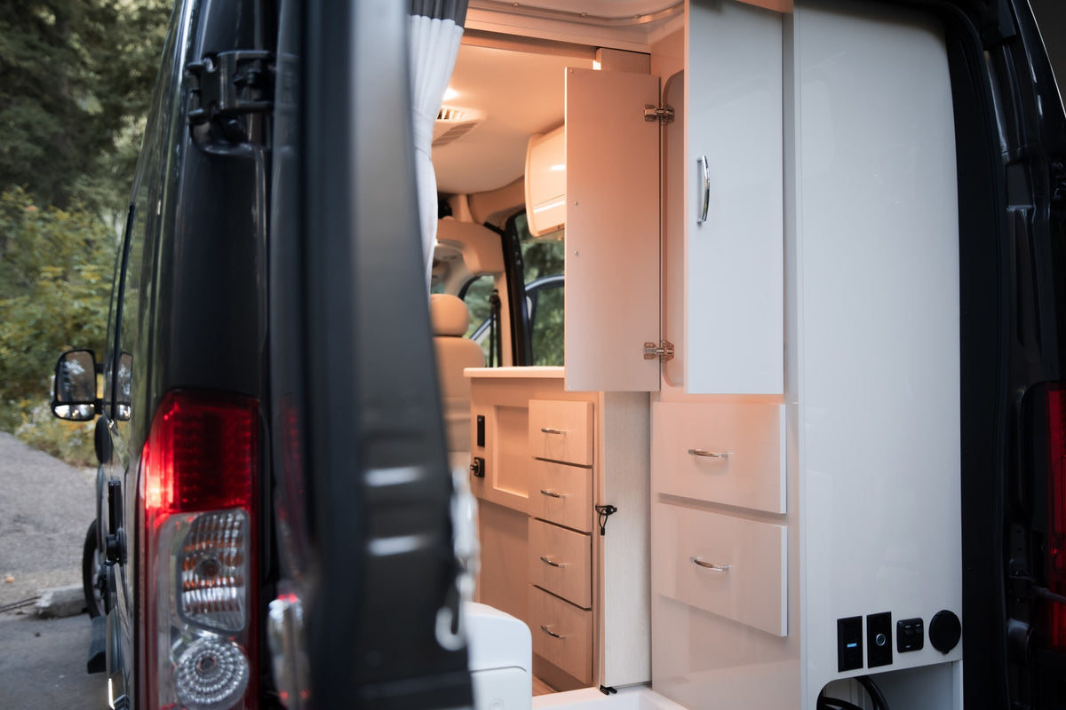 Inside an RV rental: a bright camper van interior with modular storage, light wood and white cabinetry, seen from the rear. — photo 16