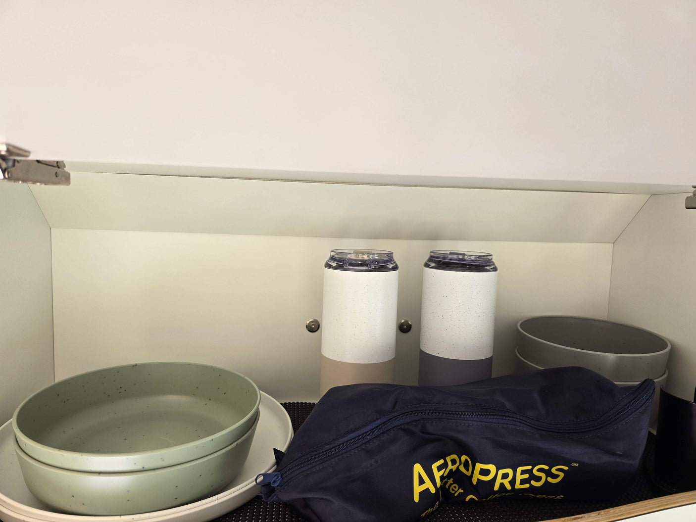 Organized RV rental kitchen cabinet featuring an Aeropress, travel mugs, and stackable bowls.