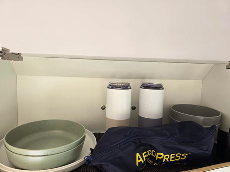 Organized RV rental kitchen cabinet featuring an Aeropress, travel mugs, and stackable bowls.