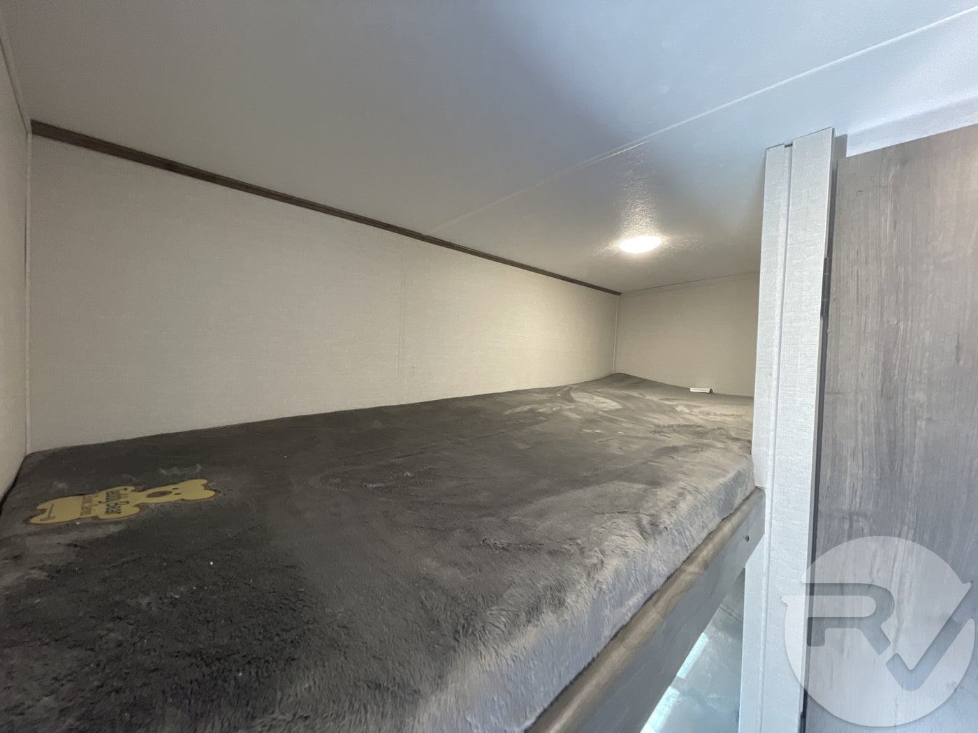 Cozy RV rental bunk bed interior, featuring a plush grey mattress, overhead light, and Safety Bear sticker. — photo 14