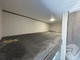 Cozy RV rental bunk bed interior, featuring a plush grey mattress, overhead light, and Safety Bear sticker.