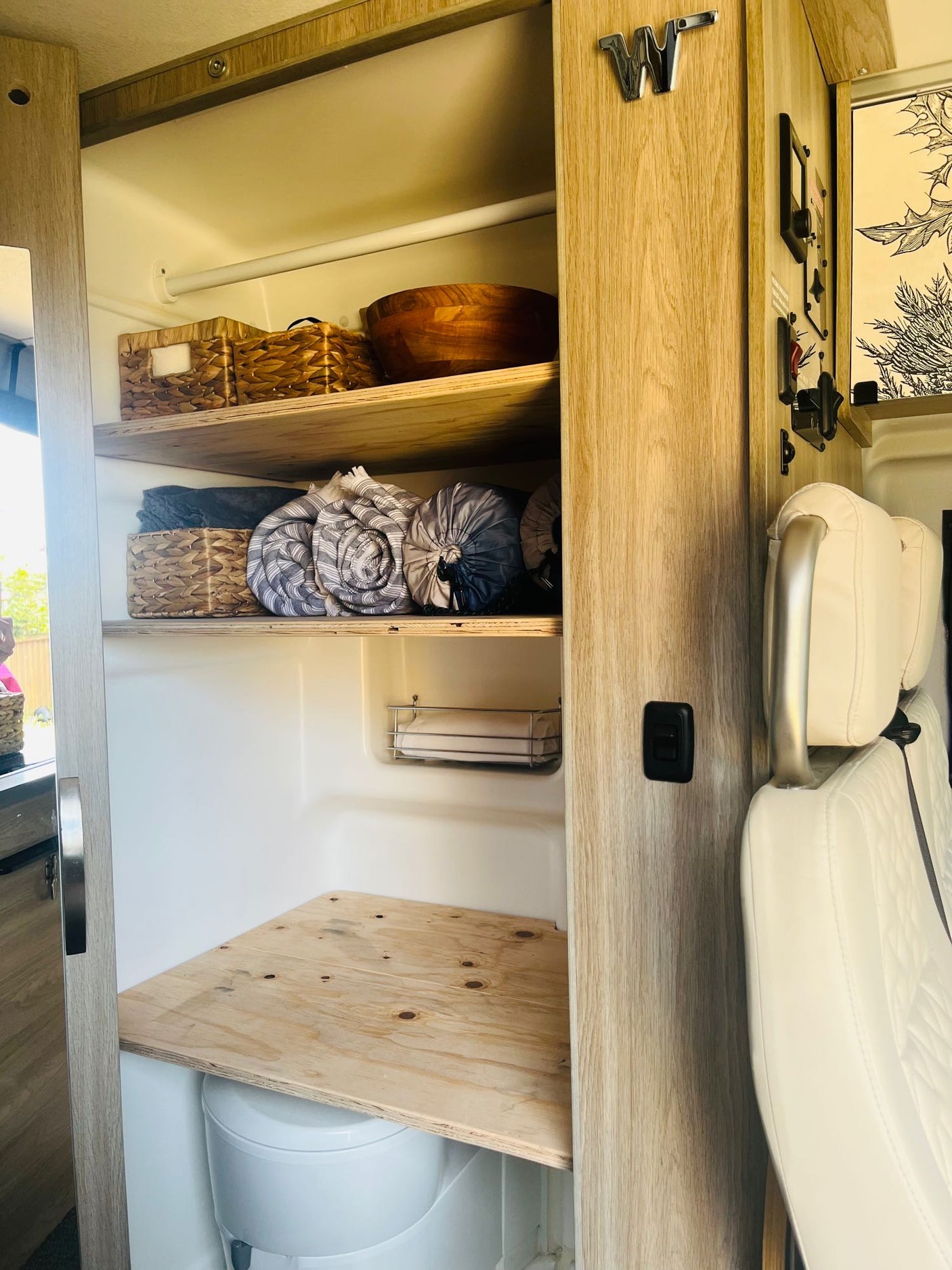 This rv rental showcases efficient storage with open shelves holding blankets, baskets, and a visible toilet, plus seating for convenience.