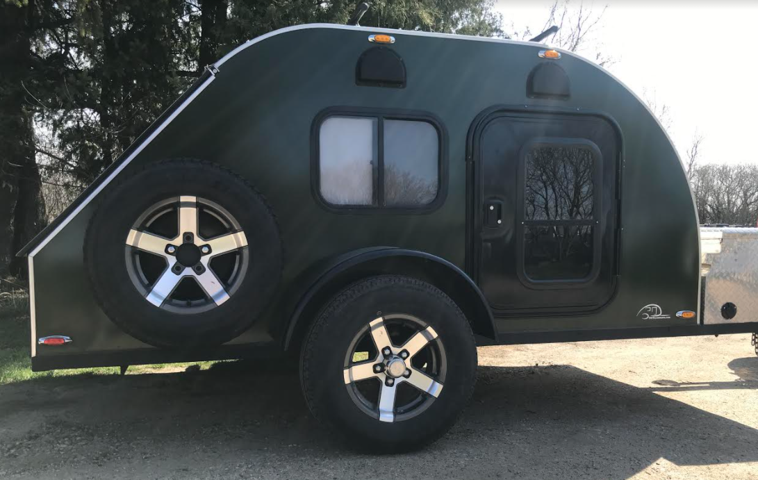 This dark green teardrop travel trailer is an ideal RV rental, featuring a rear spare tire and side entrance.