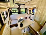 RV rental interior: comfortable dinette with laptop & mug on light-colored seating, offering outdoor views.