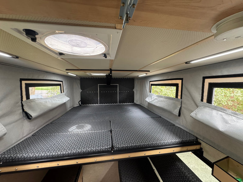 and open rear door revealing bikes and gear storage.|Enter this inviting RV rental: a compact camper interior with a bed — photo 12