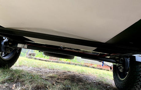 View of an RV rental's rugged underside: heavy-duty chassis, axle, off-road tires, and spare tire storage.