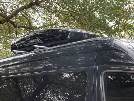 Dark-colored **rv rental** van with a Thule roof cargo box and roof racks. Ideal for travel and gear storage.