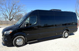 Black Sprinter-style RV rental van, parked on gravel in daylight with trees in background, ready for adventure.