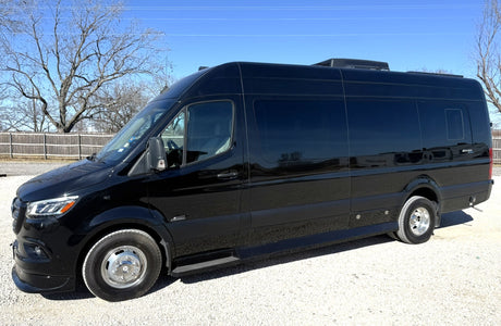 Black Sprinter-style RV rental van, parked on gravel in daylight with trees in background, ready for adventure.