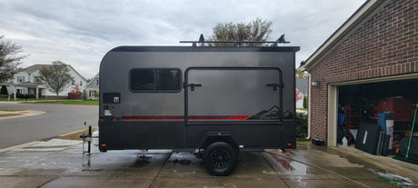 This stylish gray camper trailer, great for an rv rental, is shown freshly washed on a driveway next to a brick garage.