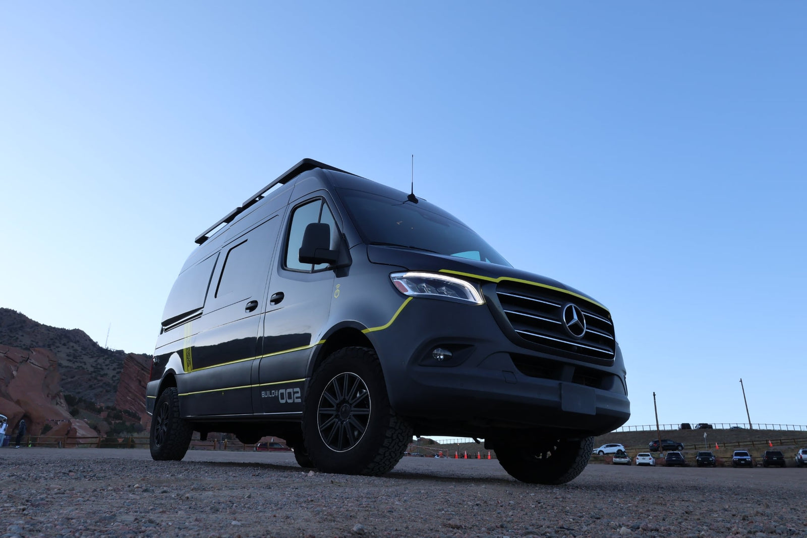 Custom black Sprinter van with yellow accents, perfect for an rv rental adventure. Parked outdoors with mountains visible.