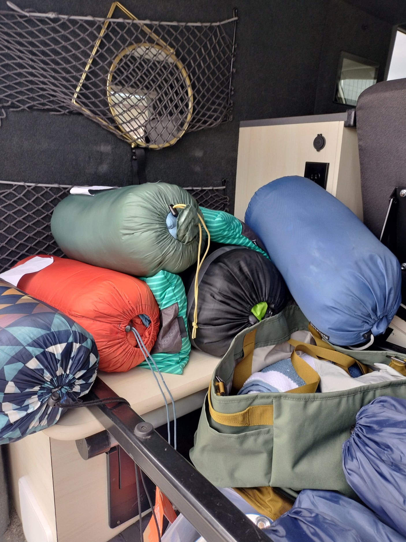 Packed RV rental interior with colorful sleeping bags, a gear bag, and storage net on the wall.