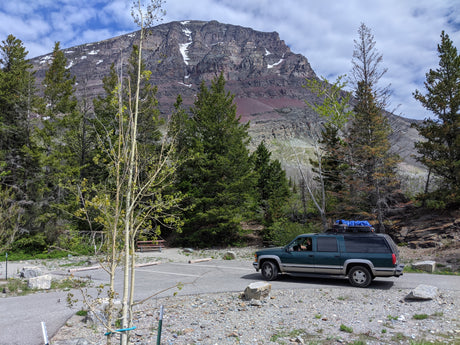 Dark green SUV with roof gear on a mountain road, perfect for an outdoor adventure, like an RV rental journey through rocky peaks.