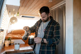 Man pouring coffee in a sunlit RV rental, showcasing its cozy wooden interior with a bed and kitchen counter.