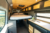 RV rental: Modern camper van interior featuring an elevated bed, kitchenette, wood ceiling, and window view of nature.