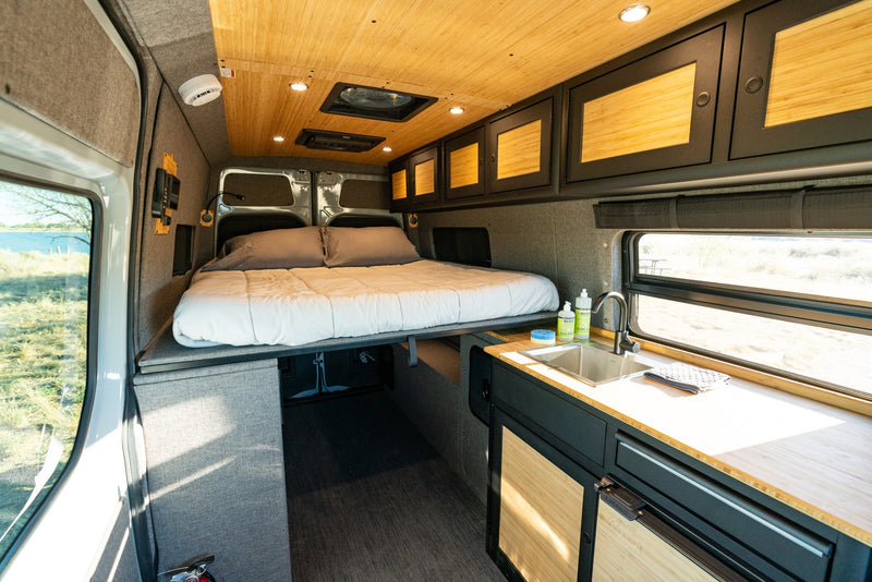 RV rental: Modern camper van interior featuring an elevated bed, kitchenette, wood ceiling, and window view of nature. — photo 11
