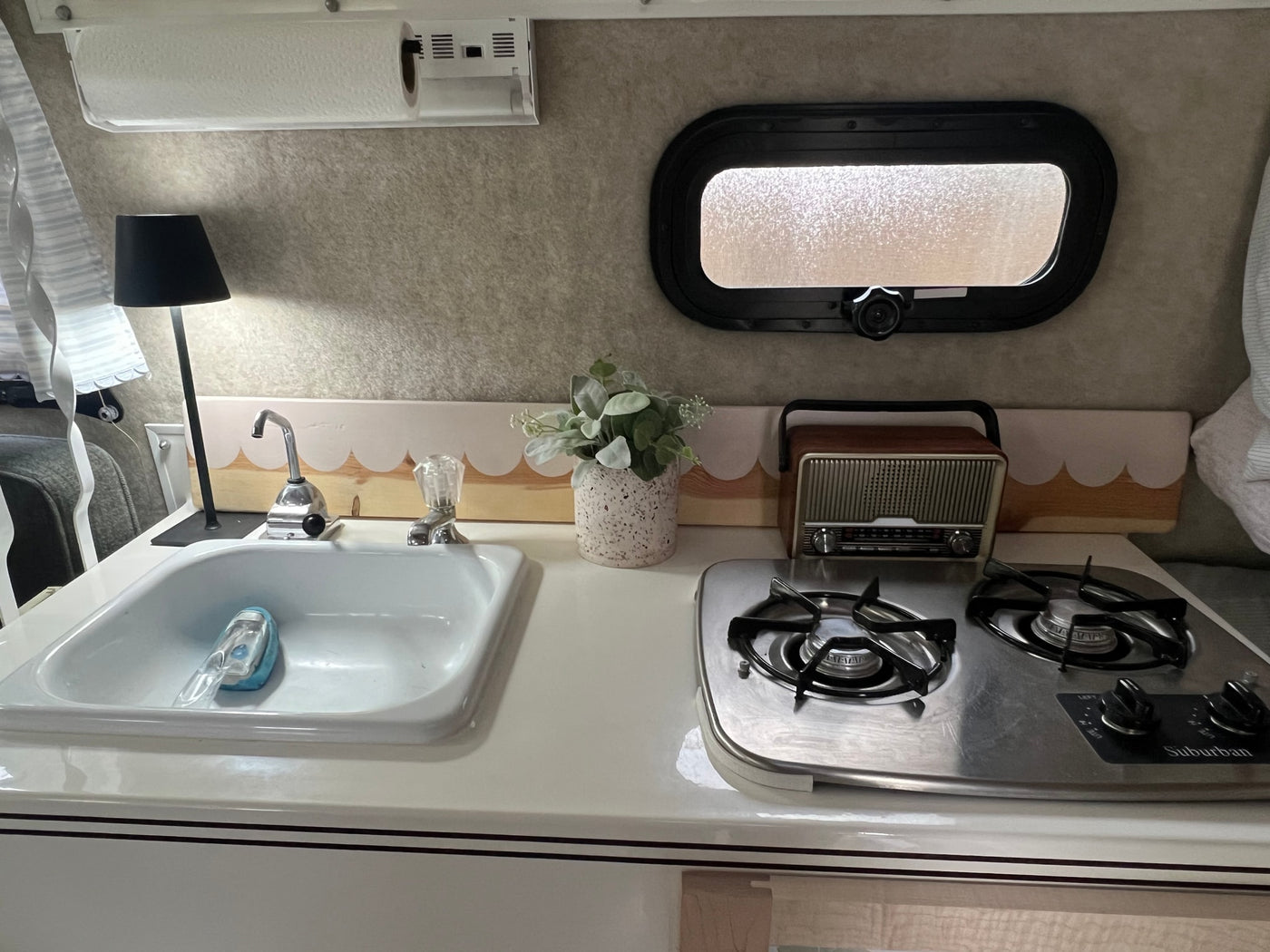 This rv rental's compact kitchen has a sink, two-burner stove, paper towel holder, window, and decorative backsplash. — photo 13